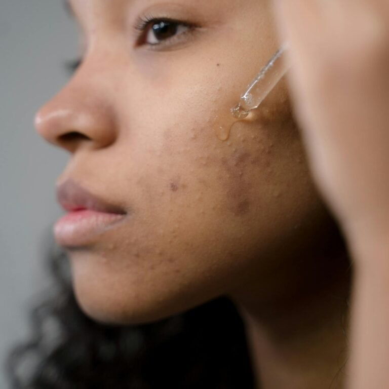 Close-up side view of a woman applying serum to her skin in a studio setting.