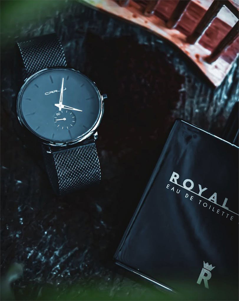 Close-up of a luxury wristwatch paired with Royal eau de toilette on a textured surface.